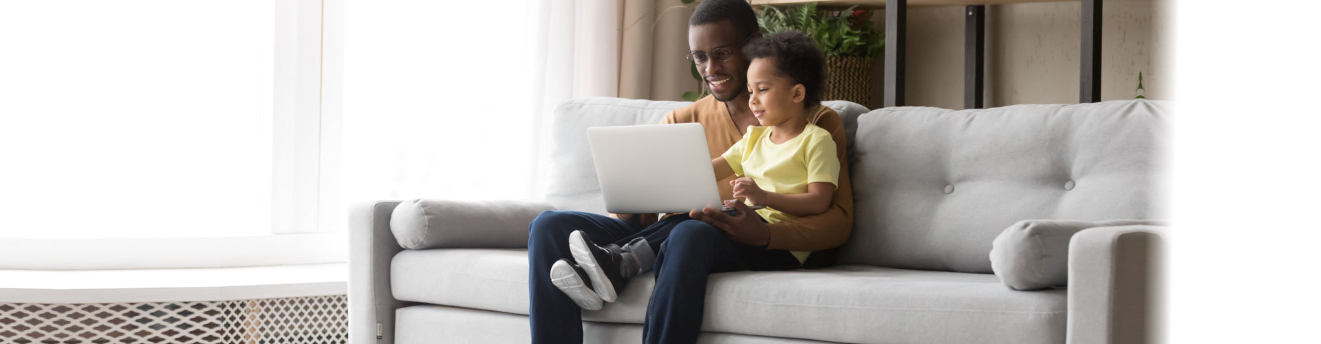 Young black father and kid son using laptop at home